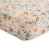 The mushie Extra Soft Muslin Crib Sheet features a colorful space-themed pattern with rockets, planets, stars, and moons in orange, blue, yellow, and green on white—perfect breathable bedding for babies.