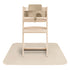 A light wooden high chair with a beige baby seat insert sits on a large Mushie Splat Mat in Fog, shown from the front.