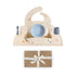 The mushie Stage 1 Dinos Feeding Kit features a beige silicone bib, bowl, cup, spoon, and fork with colorful dinosaur designs on a matching placemat. Below sits a brown gift box with a white “mushie” ribbon.