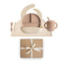 The mushie Stage 2 Natural/Shifting Sand Feeding Kit, featuring a beige silicone plate, bowl, bib, training cup with straw, spoon, and fork on a mat, is shown above a brown gift box with a white ribbon.