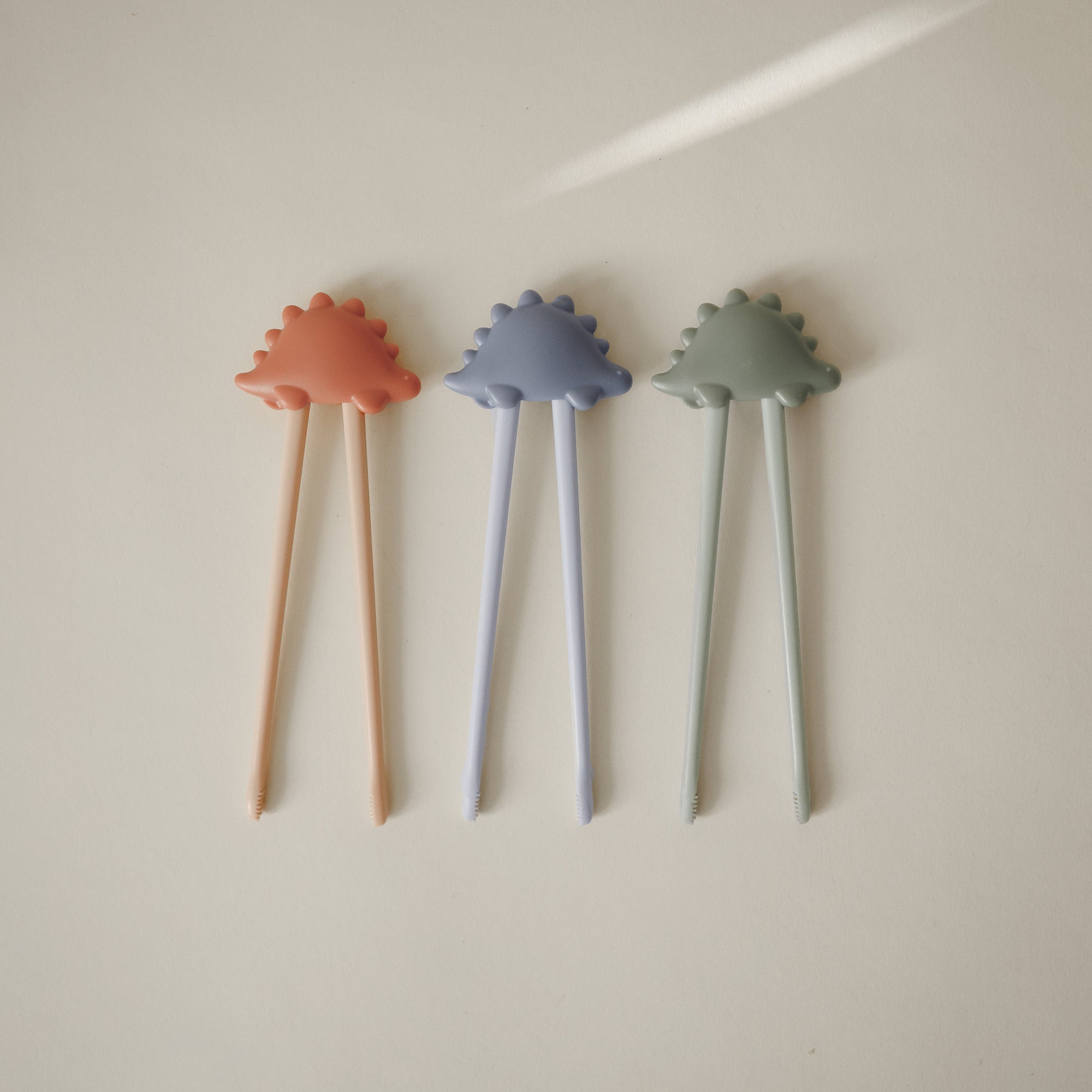 Three mushie training chopsticks for toddlers in pastel colors on a light background.