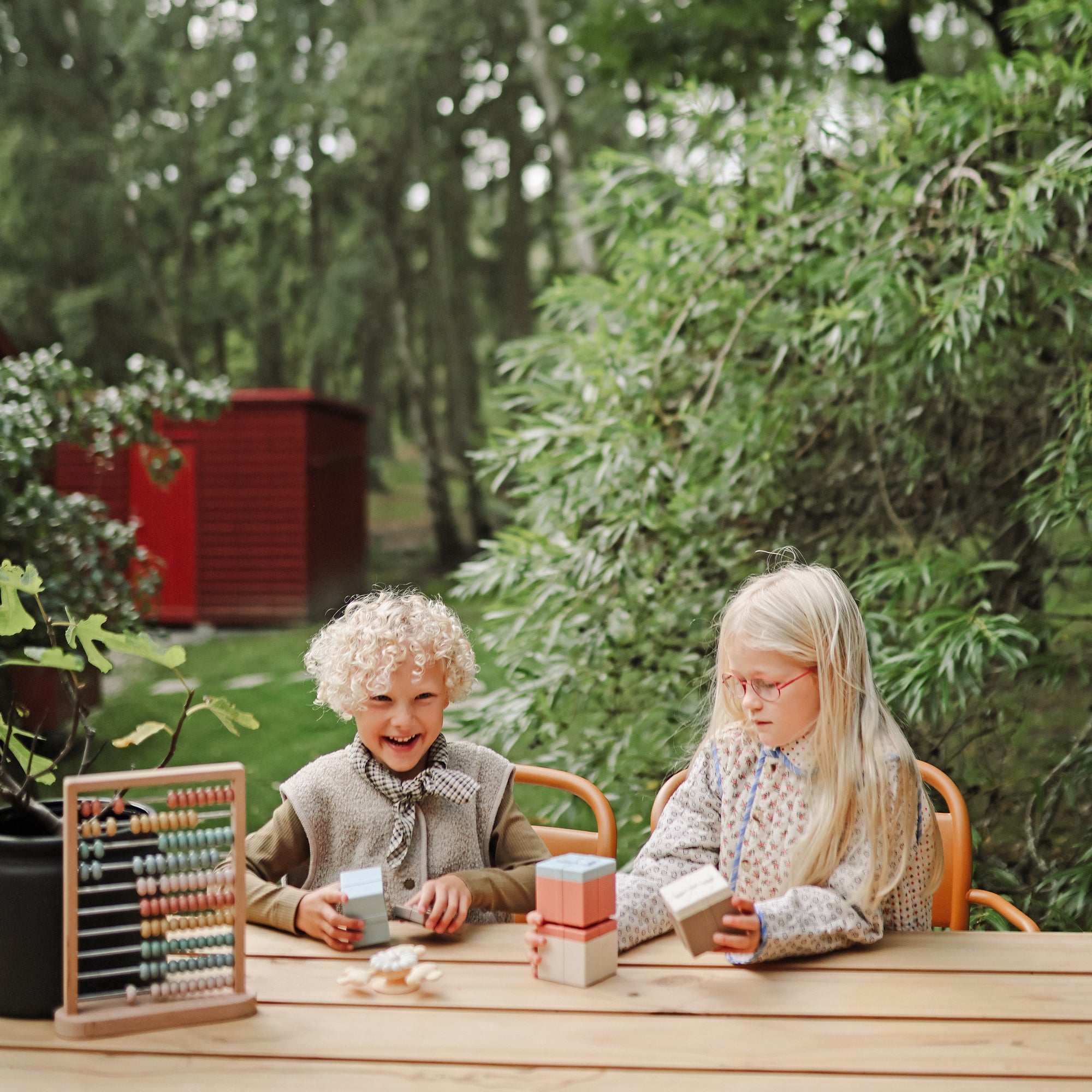 Two children play with mushie Mix and Match Toy at a wooden outdoor table.