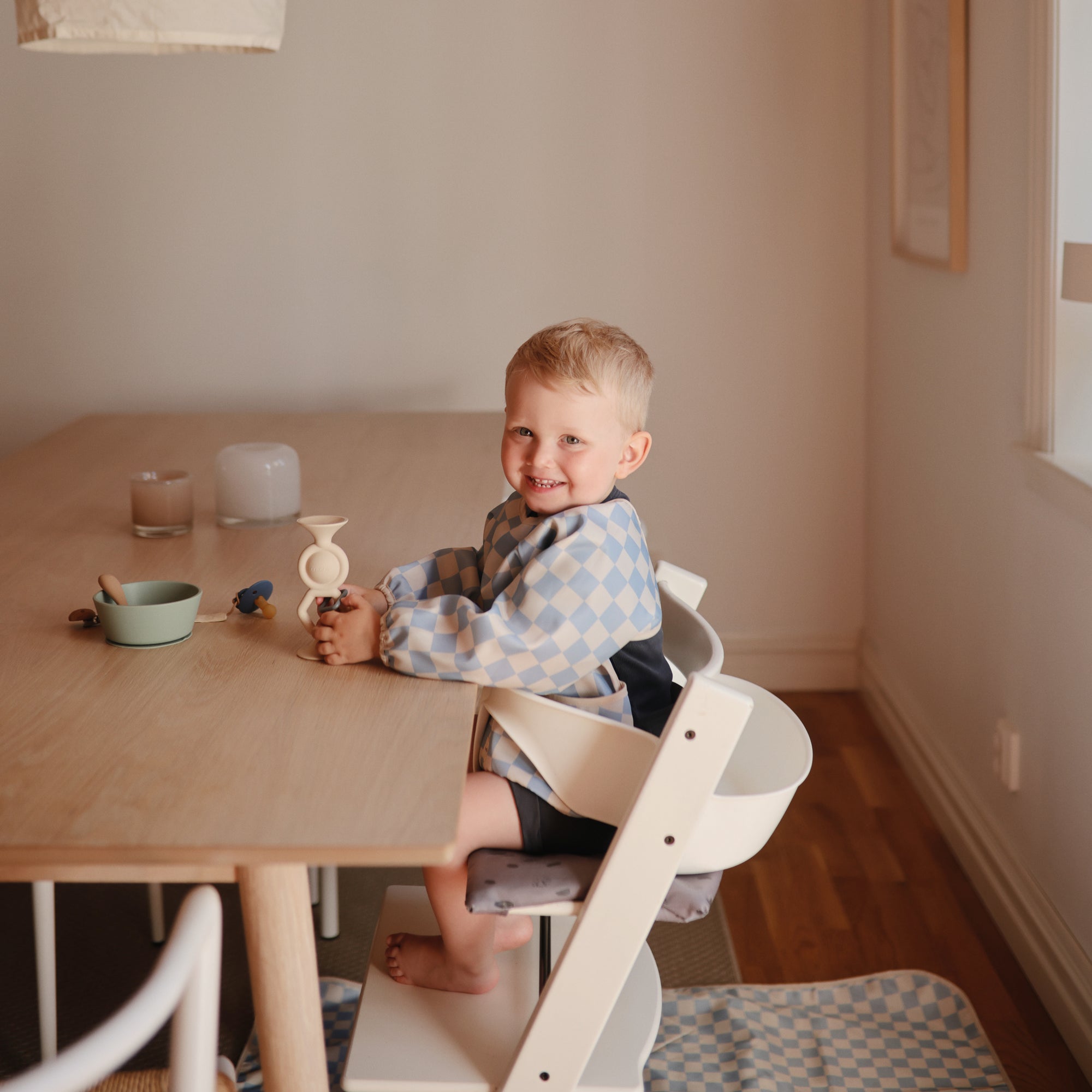 Smiling toddler plays with a mushie HexaPop Suction Toy in a high chair at the table.