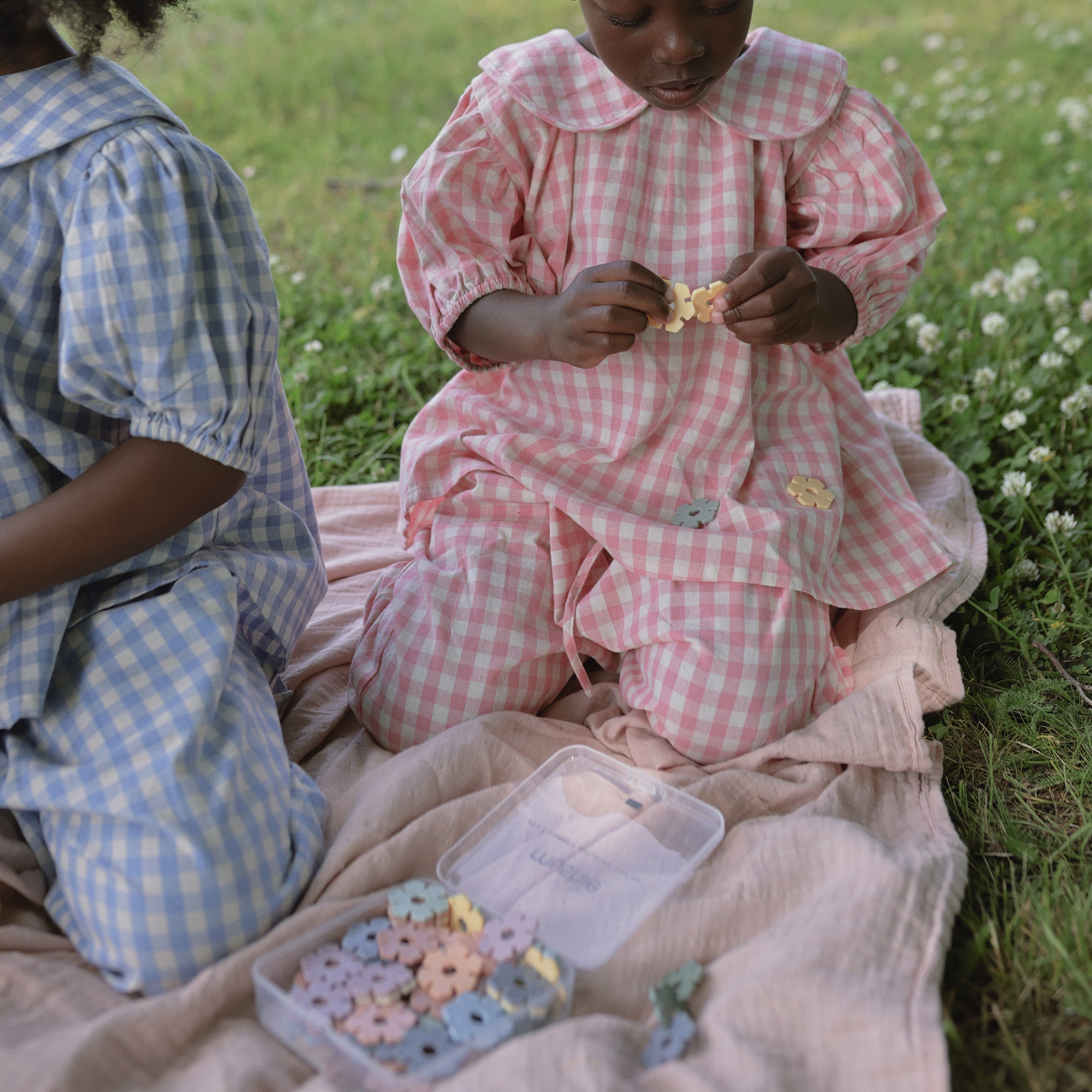Two children play on a mushie Organic Cotton Muslin Swaddle Blanket with flower-shaped beads.