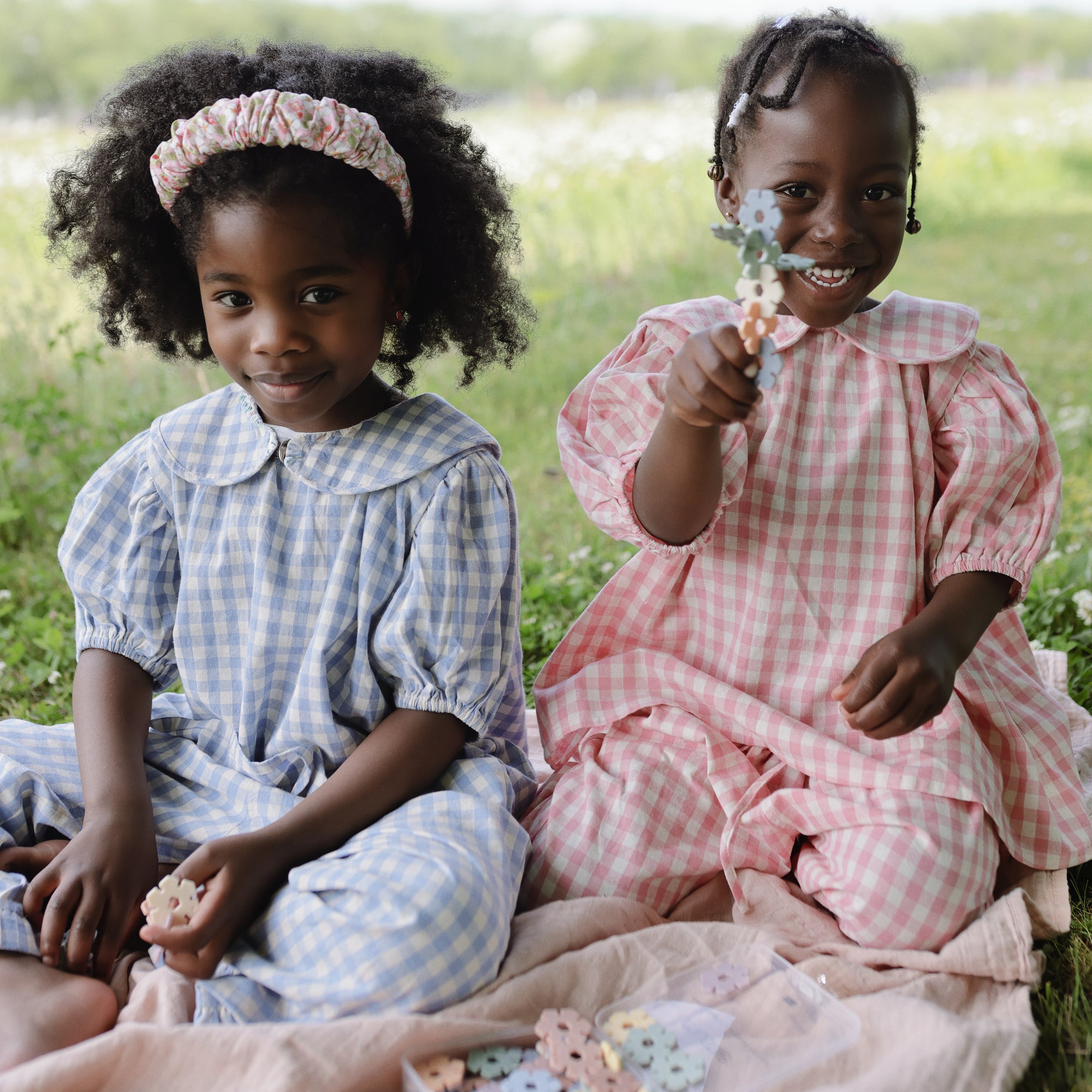 Two girls play with the mushie HEX Connect Building Toy Set, smiling on a picnic blanket.