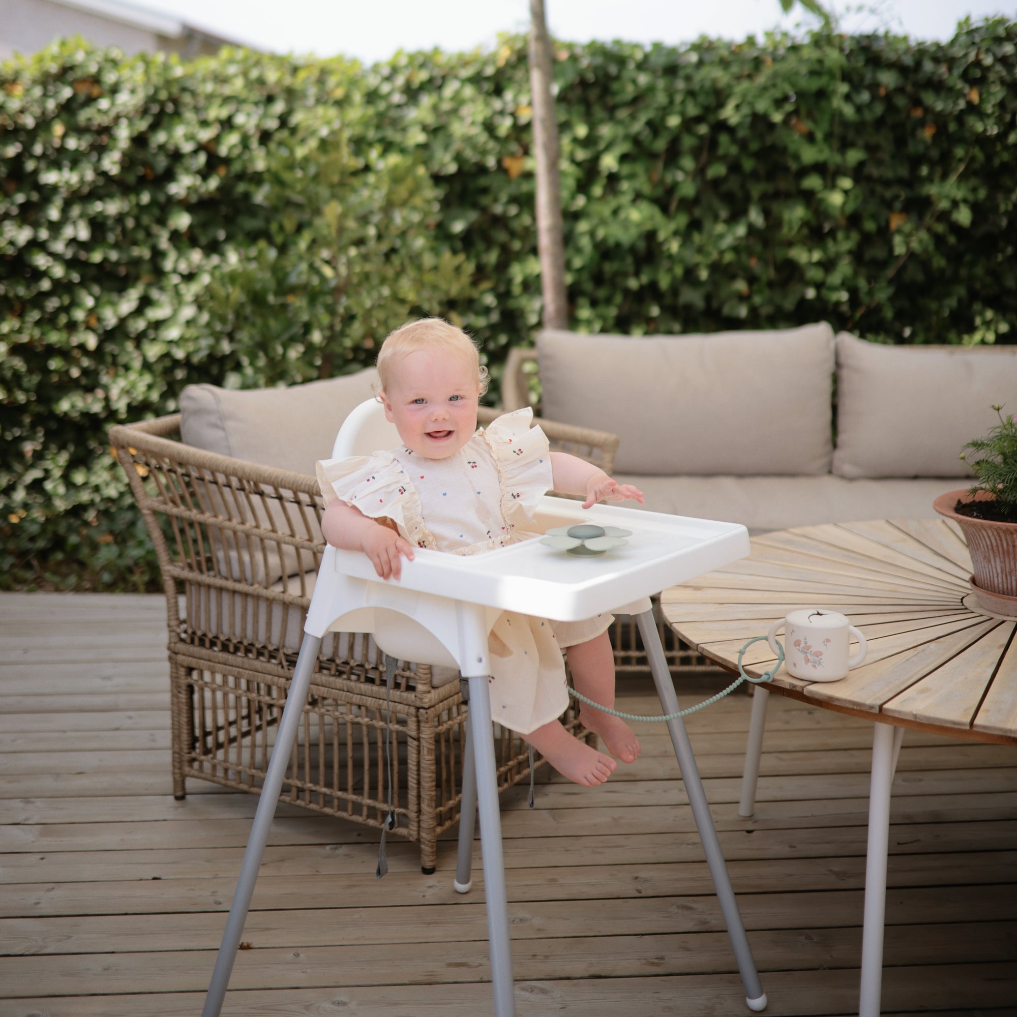 Smiling baby in a high chair with mushie Adjustable Silicone Strap 2-Pack on a patio.