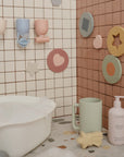 Mushie Baby Shampoo & Body Wash beside children’s bath toys and cups on a tiled ledge.