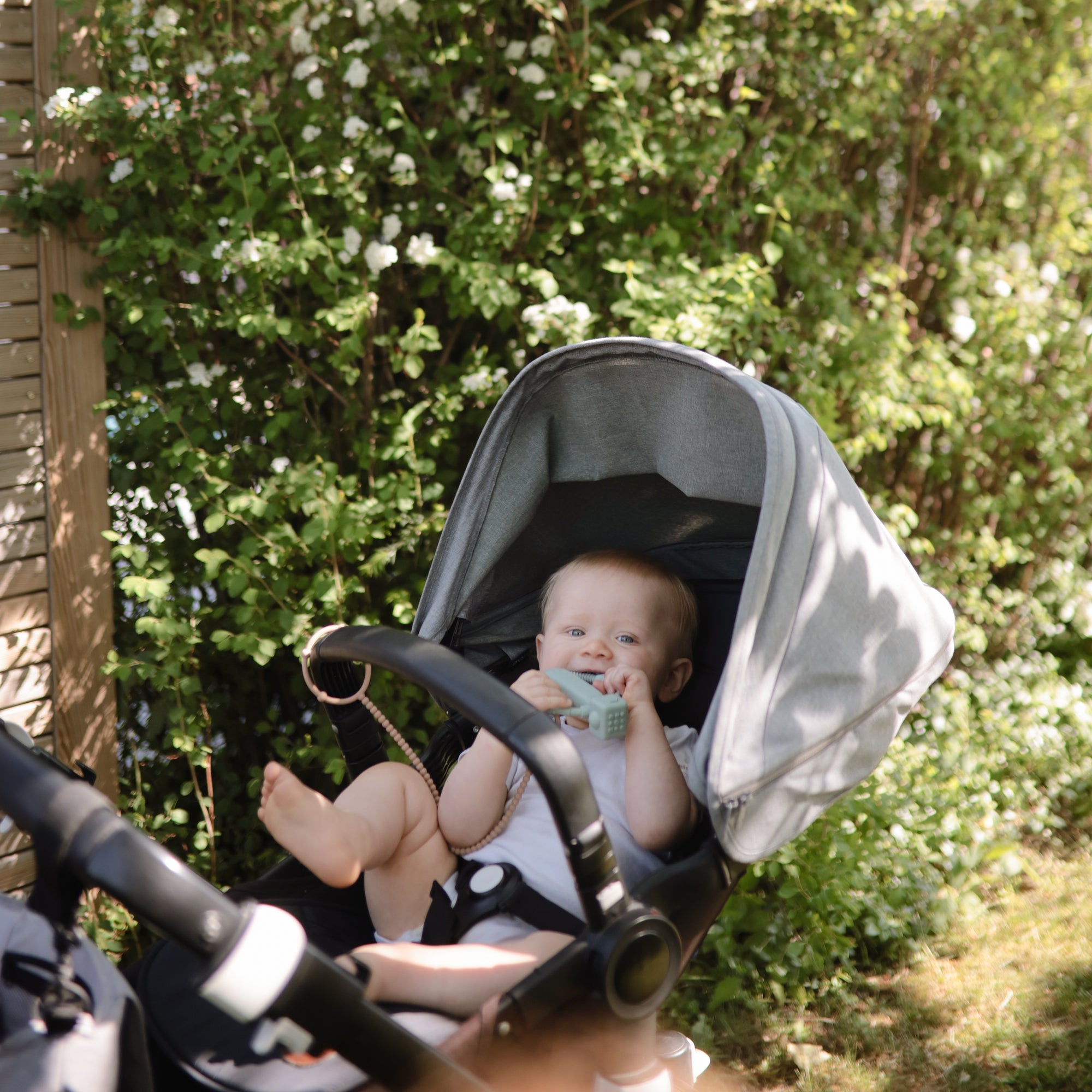 A baby uses the mushie Adjustable Silicone Strap 2-Pack while sitting in a stroller outside.
