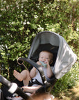 A baby uses the mushie Adjustable Silicone Strap 2-Pack while sitting in a stroller outside.