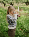 A child plays in a sweater with mushie Kaleidoscopes in a grassy orchard.