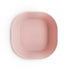 A light pink, square BPA-free silicone bowl from mushie's Square Dinnerware Bowls collection features rounded edges and an embossed brand name in the center, shown from above on a white background.