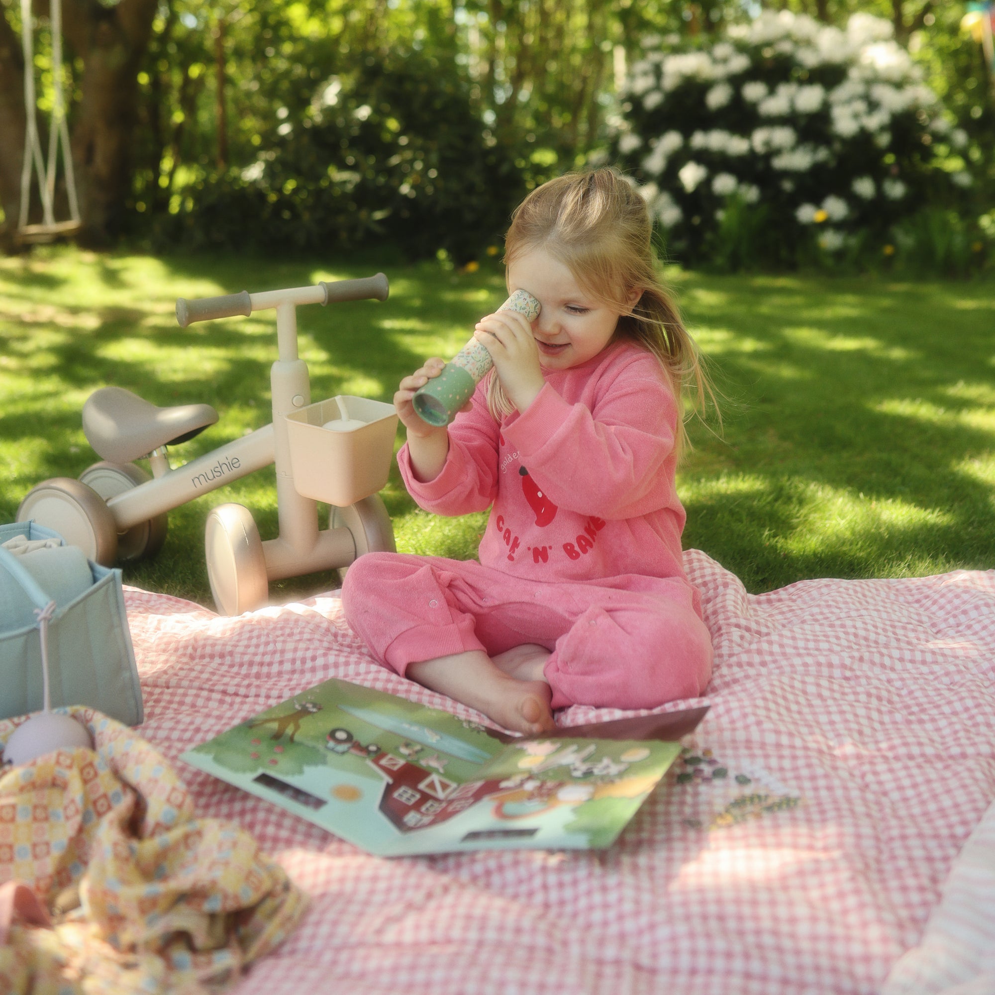 Young girl in pink pajamas plays with mushie Reusable Sticker Set on a picnic blanket.