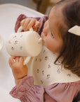 Toddler uses Rylee + Cru Feeding Kit Heart Ditsy bib, sipping from cup in highchair.
