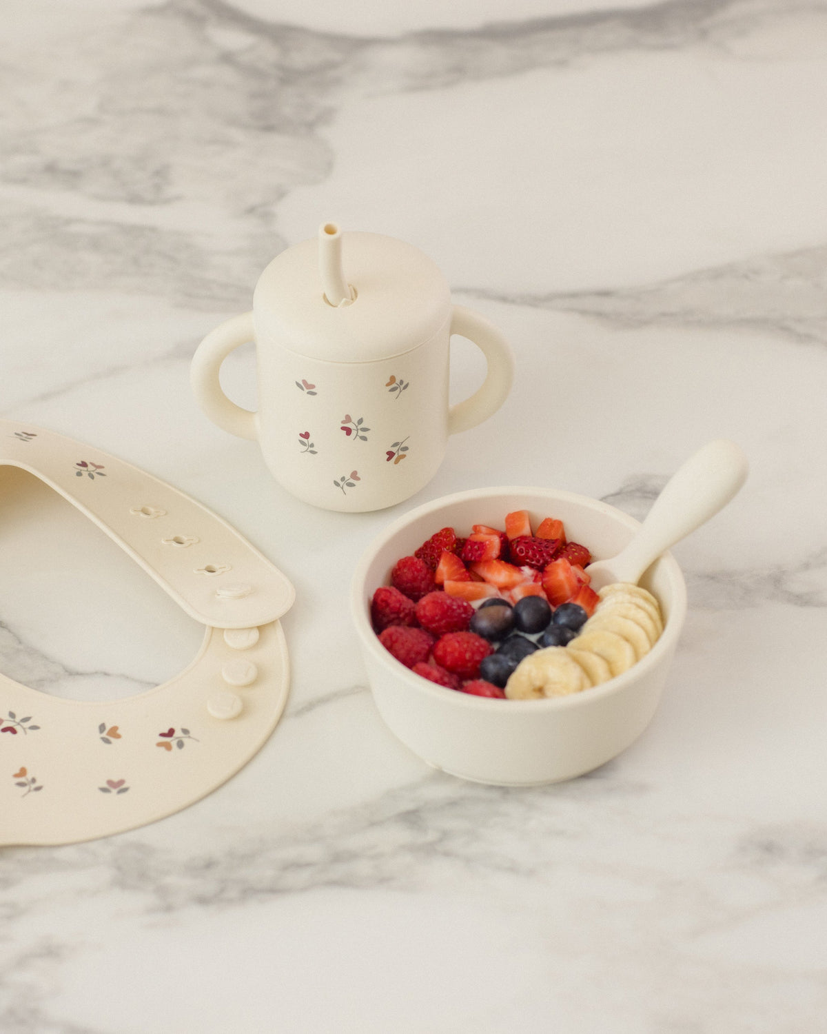 Rylee + Cru Feeding Kit Heart Ditsy with bowl, cup, spoon, bib &amp; fruit on marble.