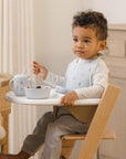 Toddler uses Rylee + Cru Feeding Kit Space—bowl, cup & spoon—while sitting in high chair.