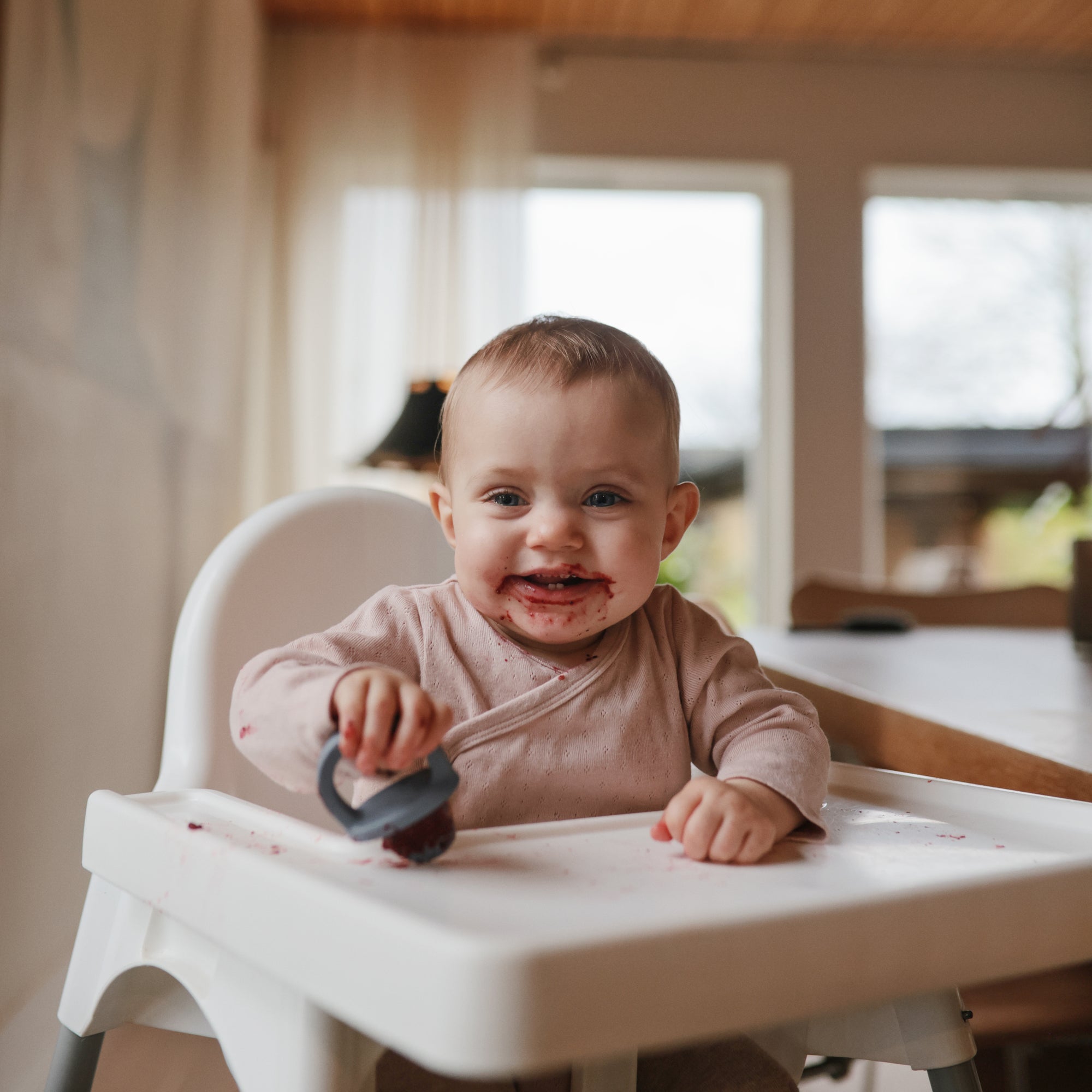 Smiling baby with food, holding mushie Toddler Ice Pop Tray, dishwasher safe and toddler-friendly.