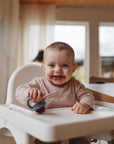 Smiling baby with food, holding mushie Toddler Ice Pop Tray, dishwasher safe and toddler-friendly.
