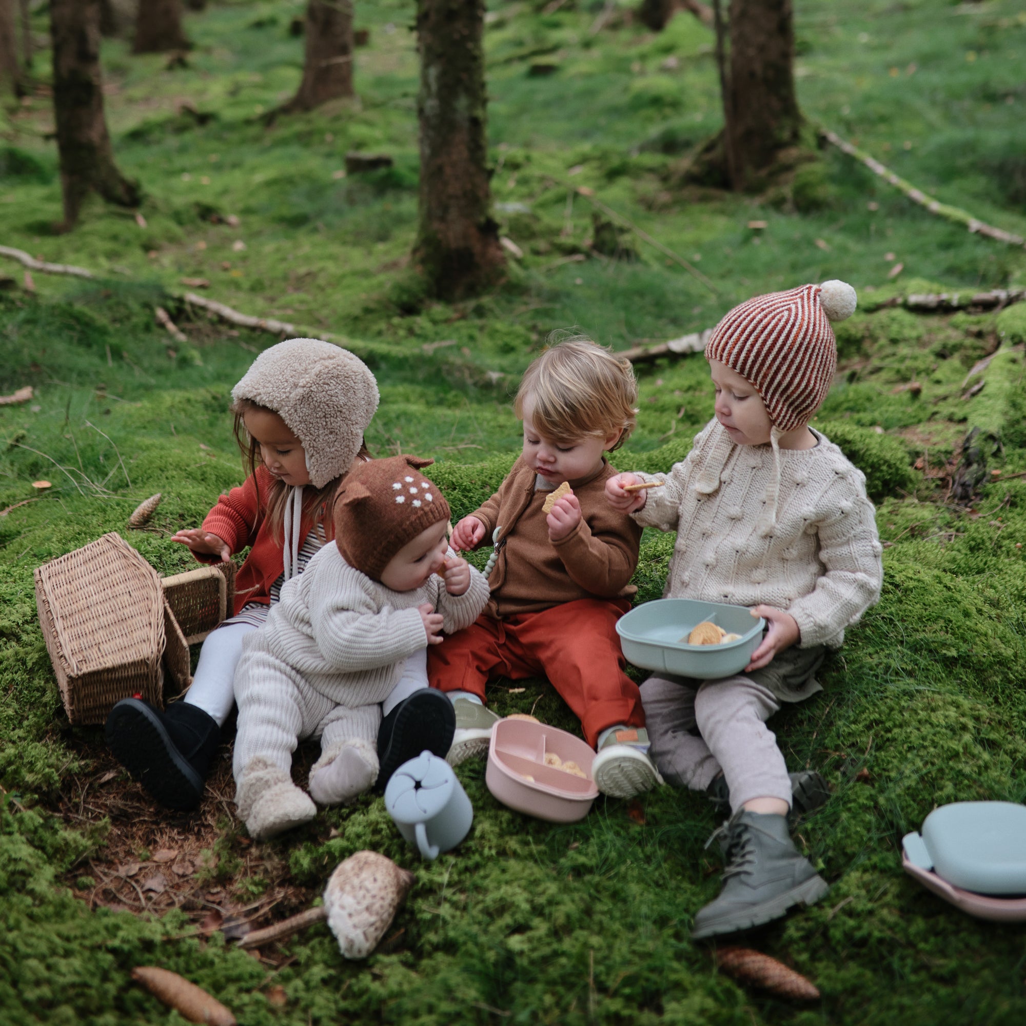 Four kids share snacks from mushie's Lunchbox with built-in compartments while sitting on moss.