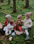 Four kids share snacks from mushie's Lunchbox with built-in compartments while sitting on moss.