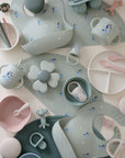 Mushie Bluey Gift Set: pastel silicone baby feeding items and toys with themed bibs displayed.