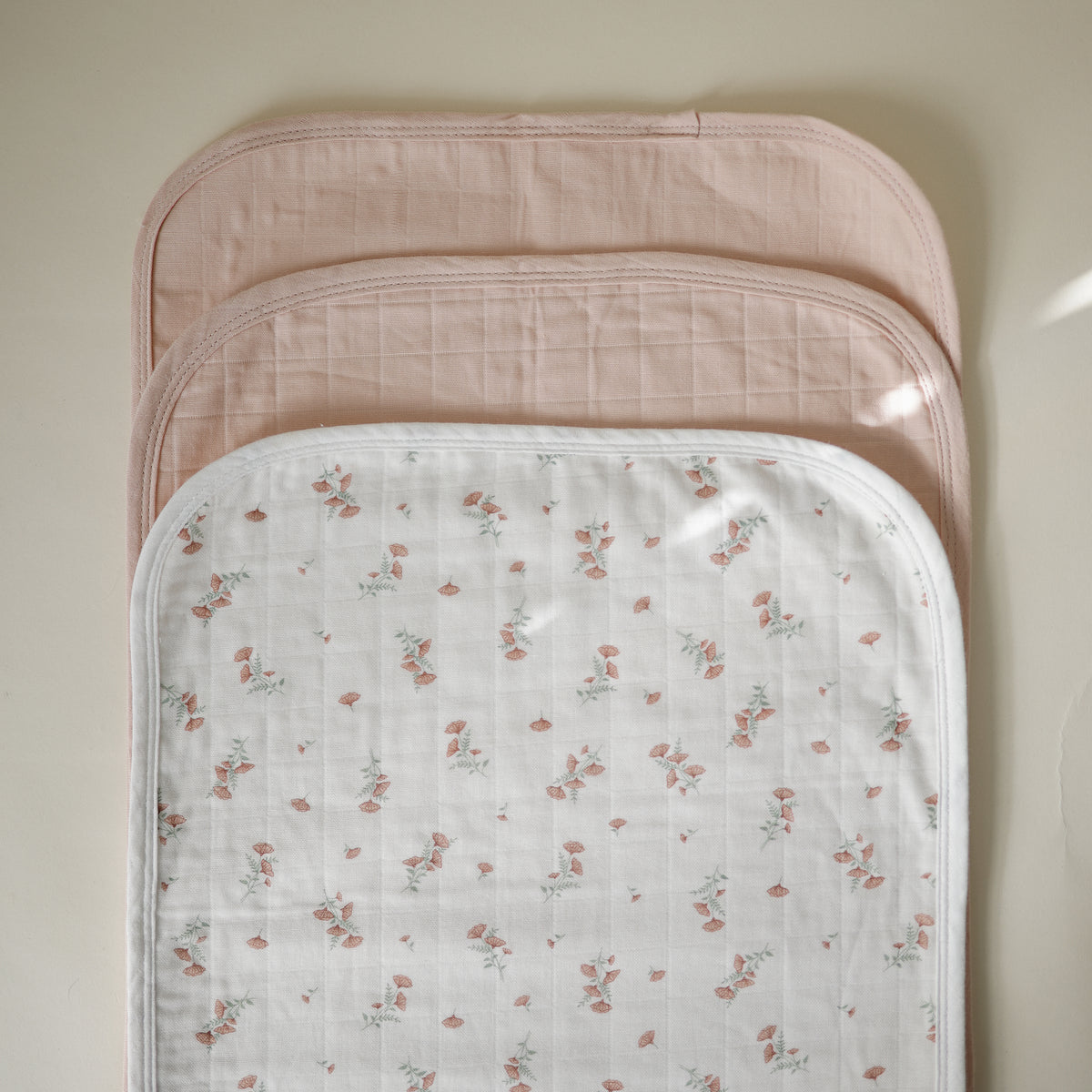 Three Mushie Changing Pad Liners: two solid pink and one white with a floral print.