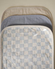 Three Mushie Changing Pad Liners in checkered, solid blue, and solid tan patterns.