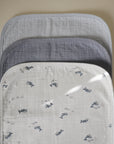 Three stacked Mushie Changing Pad Liners in white with whale patterns, grey, and light blue.