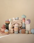 Mushie Mix and Match Toy softly arranged on beige with silicone cupcakes and a hooded towel.
