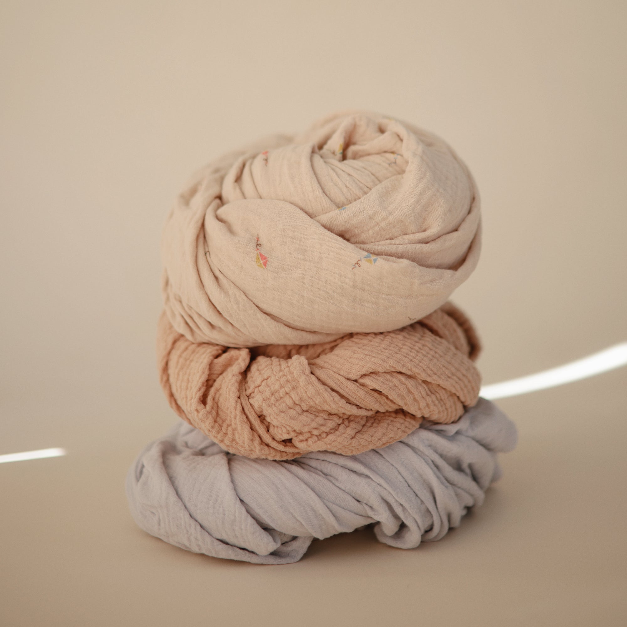 Three mushie Extra Soft Muslin Crib Sheets in neutral tones for breathable baby bedding.