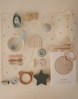 Mushie Extra Soft Muslin Crib Sheet displayed with assorted neutral baby feeding and teething items.