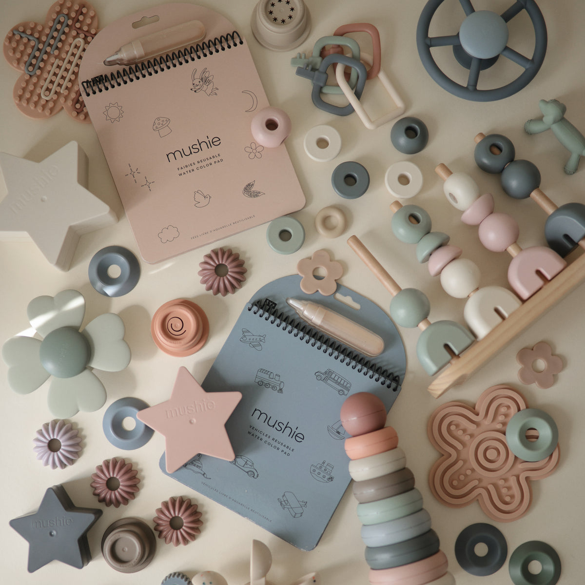 Mushie Reusable Water Color Pads and pastel baby toys arranged neatly on a light surface.