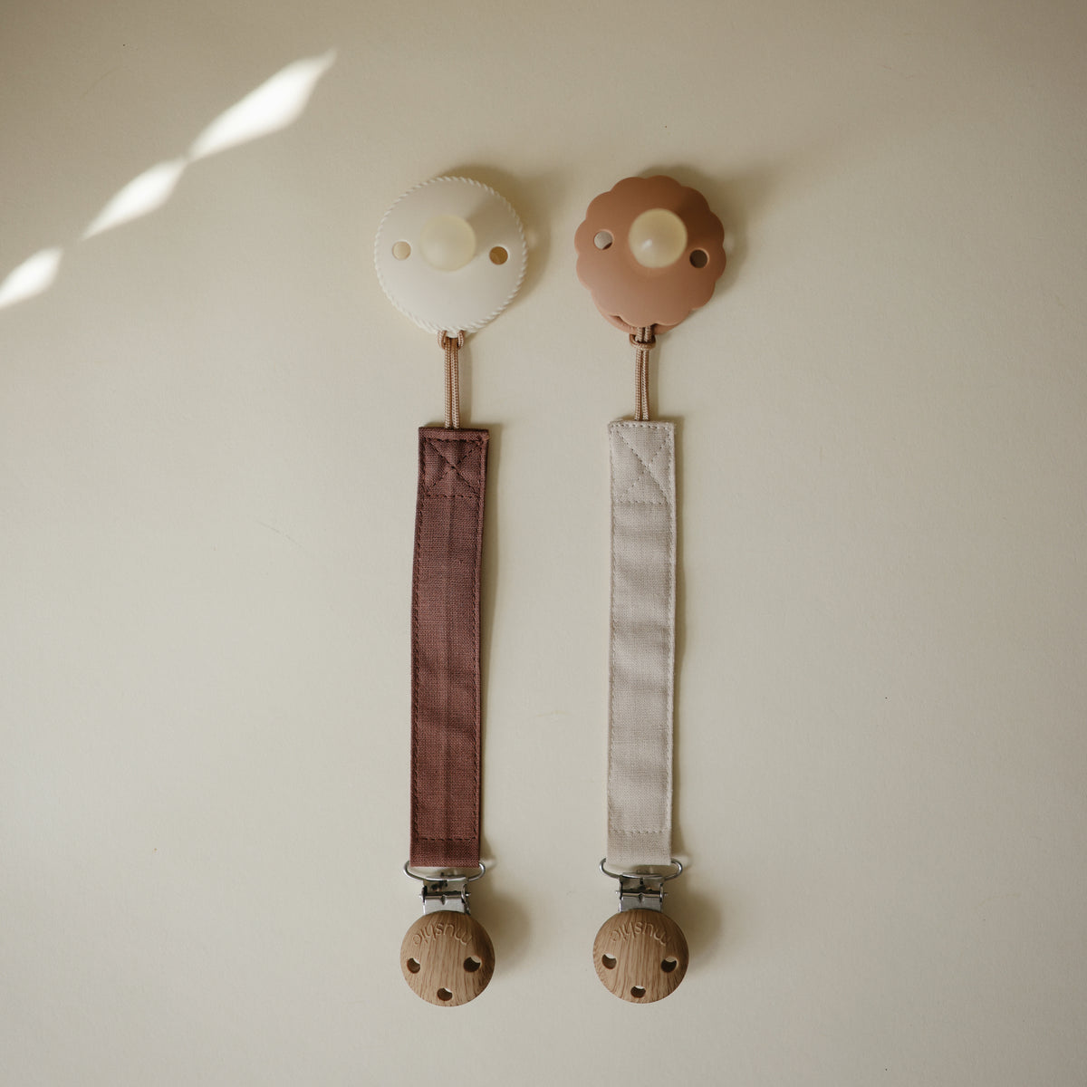 Mushie Linen Pacifier Clip 2-Pack with wooden clasps, includes one brown and one beige.