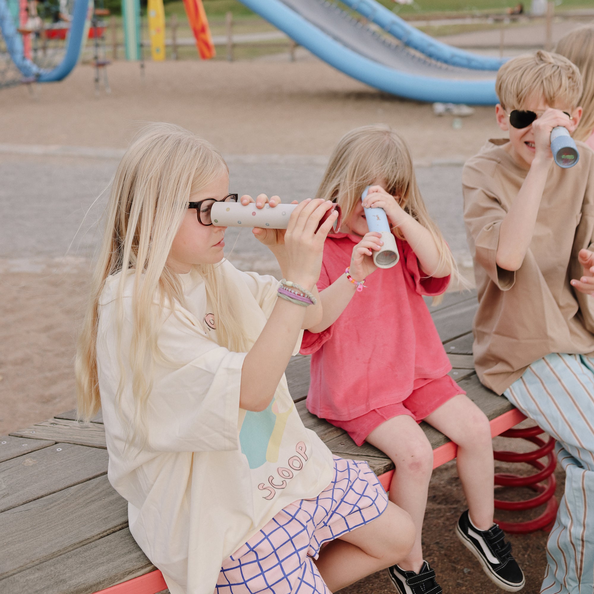 Three kids on a bench enjoy play with mushie Kaleidoscopes.