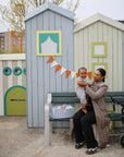A woman sits with a toddler beside a mushie Diaper Caddy on a bench.