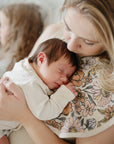 Mother kissing newborn on mushie Organic Cotton Muslin Burp Cloth 2-Pack with floral pattern.