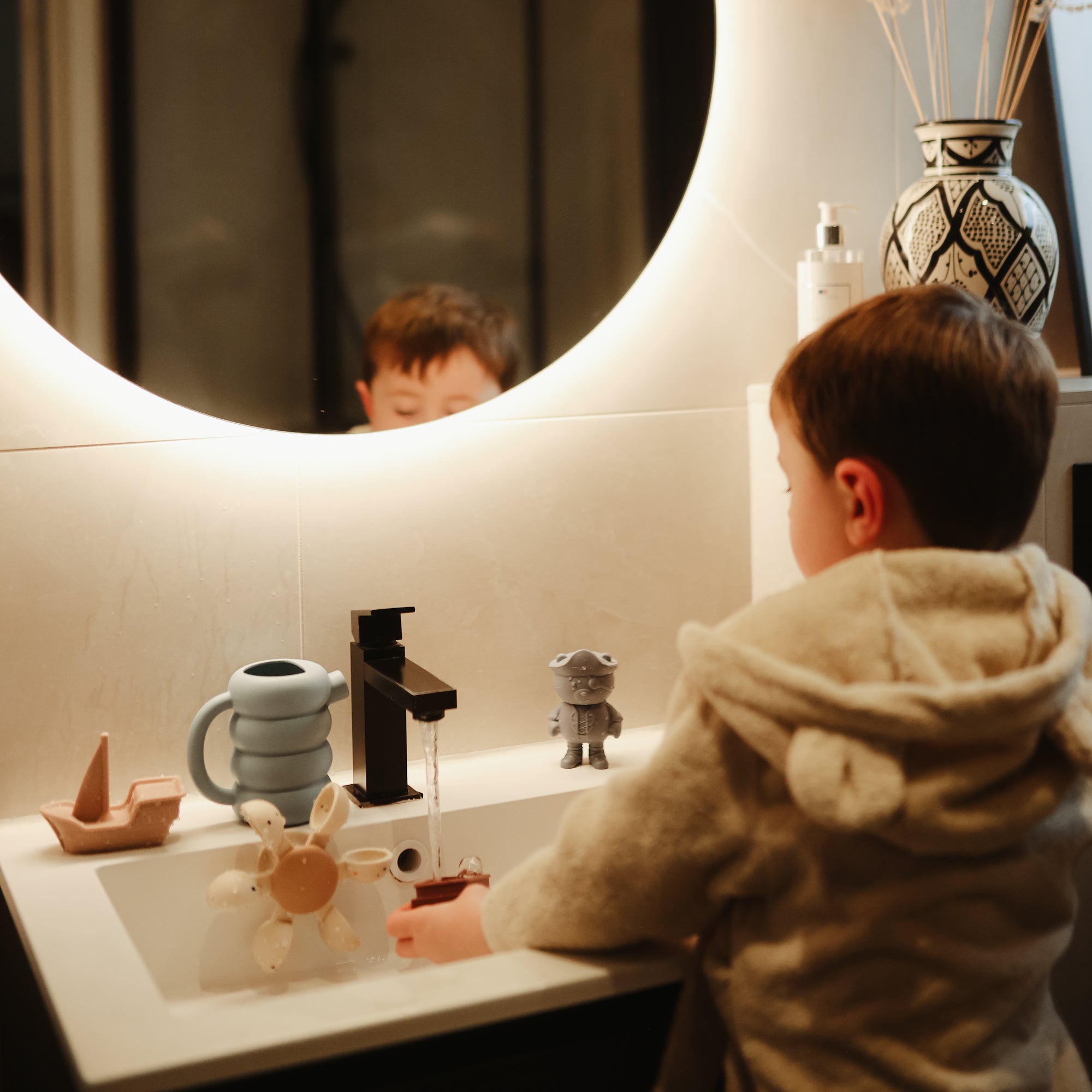 Lifestyle image of a child playing with bath toys in a sink, including the mushie Water Wheel Bath Toy and the Pirate Bath Play SEt.