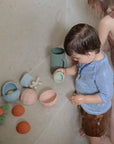 Two young children play with mushie Nesting Spheres Sensory Toy in pastel colors in a shower.