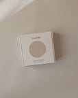 A mushie Stretchy Swaddle box with a circular window sits on a beige surface.