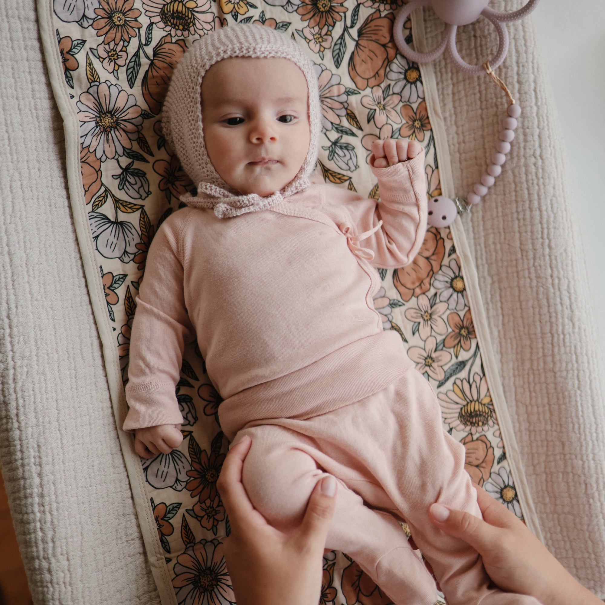 Baby in pink on floral blanket, resting on Mushie Changing Pad Liners.
