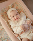 Baby on floral blanket with Mushie Changing Pad Liners, in cream bonnet and outfit.