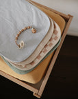 Mushie Changing Pad Liners stacked with a pacifier on a wooden changing table.