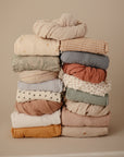 The mushie Mini Muslin Crib Sheet on a neutral background with colorful, textured baby bedding.