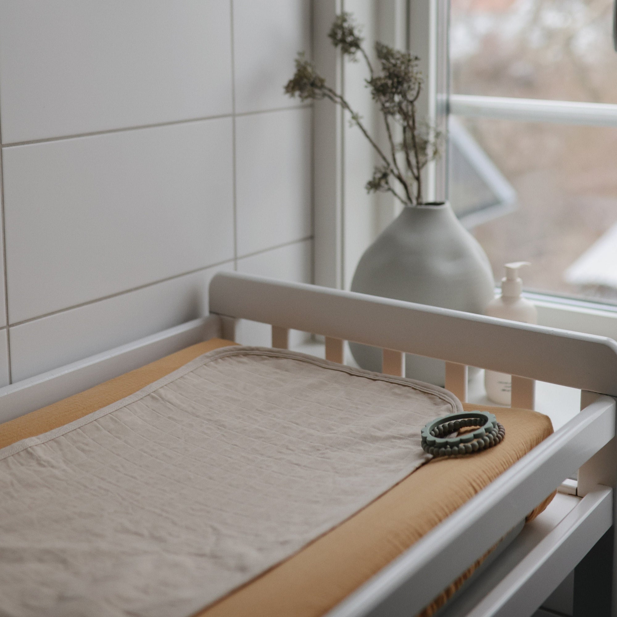 Beige mat, Mushie changing pad liners, green teething rings, and soap on changing table.