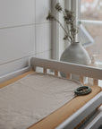 Beige mat, Mushie changing pad liners, green teething rings, and soap on changing table.