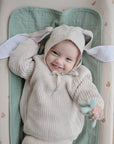 Happy baby in Mushie Changing Pad Liners and organic cotton knit suit with bunny-ear hat.