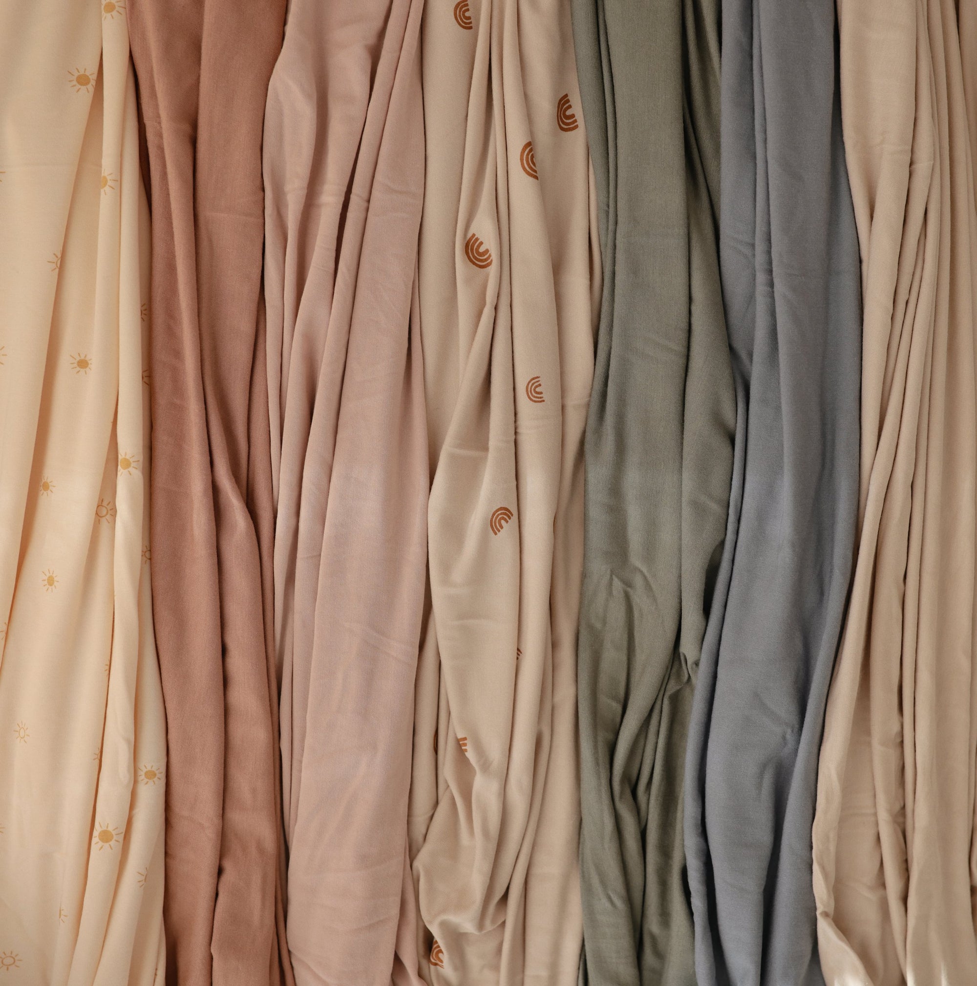 Mushie Stretchy Swaddle fabrics in soft pastels and neutrals hang with subtle patterns.