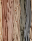 Mushie Stretchy Swaddle fabrics in soft pastels and neutrals hang with subtle patterns.