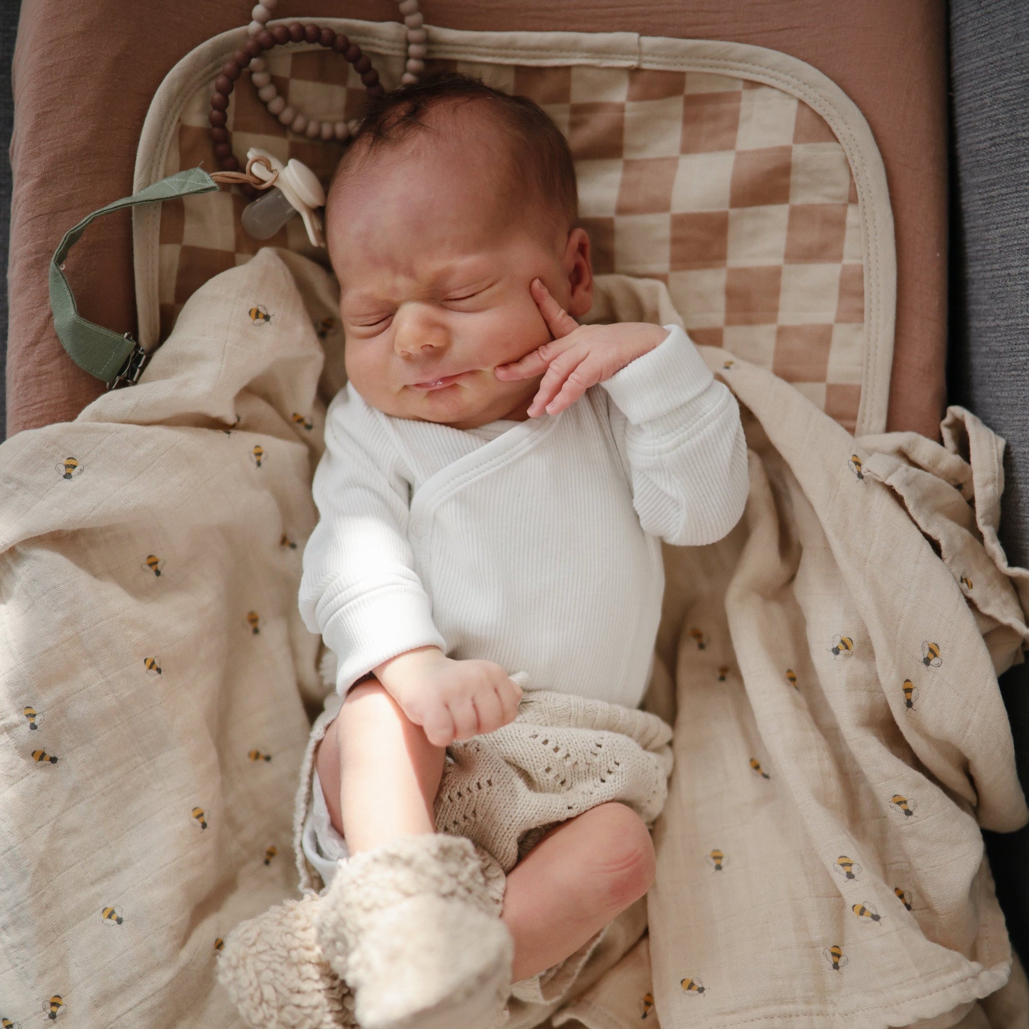 Newborn sleeping on Mushie Changing Pad Liner, in white outfit and knitted booties.