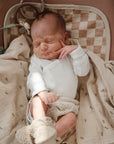 Newborn sleeping on Mushie Changing Pad Liner, in white outfit and knitted booties.
