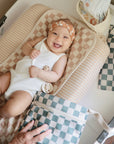 Smiling baby on Mushie Changing Pad Liners, white onesie, checkered accessories nearby.